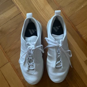 Vita sneakers i skinn med snörning - Fräscha vita sneakers från Adidas i äkta skinn med klassisk snörning och perforerade detaljer på sidorna. Snygg minimalistisk design med rund tå och vit platt sula. Perfekta för en clean och stilren look. Knappt använda.