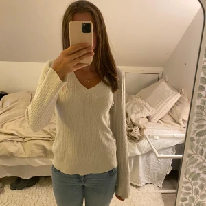 Vit kabelstickad tröja U.S polo assn - Vit kabelstickad tröja från U.S polo assn.  med v-ringning och lång ärm. Tröjan har en klassisk, smal passform och är tillverkad i en mjuk blandning av rayon, polyester och nylon. Perfekt för lager-på-lager under kyliga dagar.