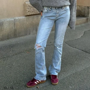 True Religion ljusa bootcut jeans - Säljer ett par ljusblå bootcut jeans från True Religion med slitna detaljer och snygga röda sömmar. Klassiska femficksmodellen med logga på bakfickan och coola knappar. Perfekta för dig som gillar en avslappnad och trendig look. Använda  3 gånger så i fint skick!