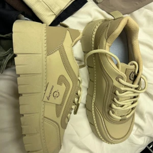 Chunky beige sneakers med plattform - Säljer ett par chunky sneakers i beige från O.X.KING. Skorna har kraftig plattformsula, rund tå och snörning. Tillverkade i syntetmaterial med coola sömdetaljer och sportig vibe. Perfekta för dig som vill sticka ut med en trendig look.