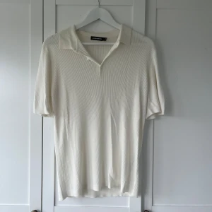 Ribbad pikétröja J.Lindeberg - Snygg och stilren piké från märket J.Lindeberg. Tröjan är ribbad och har en fin crémevit färg. Den har aldrig blivit använd och har därmed inga defekter
