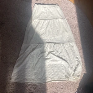 Vit långkjol med broderade detaljer Kappahl - Superfin vit långkjol från Kappahl med broderade hålmönster och volang. Kjolen har resår i midjan och är i ett mjukt bomullstyg, perfekt för en somrig look. Passar dig som gillar romantisk och luftig stil.