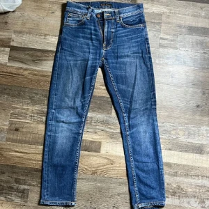 Märkblå jeans från Nudie Jeans, W28 L30 - Snygga mörkblå jeans från Nudie Jeans med klassisk femficksdesign och orangea sömmar. Jeansen har en rak passform.  Perfekta för dig som gillar en tidlös och clean look. Hör av dig vid frågor eller funderingar! 