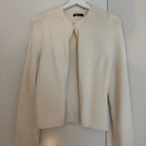 Beige kofta från Gina Tricot - En stilren beige kofta från Gina Tricot i storlek S. Koftan är stickad, har rund halsringning och stängs med en knapp upptill. Perfekt att slänga över en topp för en clean och enkel look.