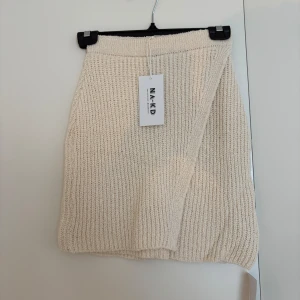 Beige stickad kjol från NA-KD - Supermysig beige stickad kjol från NA-KD i kort modell. Kjolen har ribbad struktur och elastisk midja för en bekväm passform. Perfekt att styla med en oversized tröja eller boots för en chill look. Aldrig använd.