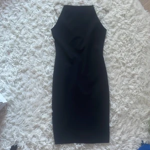 Svart klänning med glittriga band XS - Supersnygg svart klänning i figurnära modell med glittriga axelband i strass. Klänningen har en stilren, rak siluett och är ärmlös. Perfekt för dig som vill sticka ut med en elegant men enkel look.