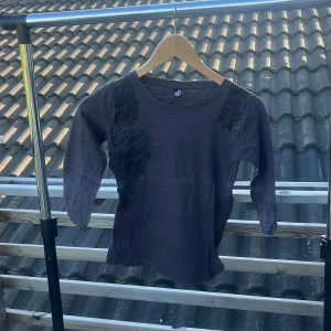 Mörkgrå bomullströja med paljettdetaljer - Snygg mörklila tröja i 100% bomull från B med trekvartsärm och coola svarta paljettdetaljer på axlarna. Tröjan har en rund halsringning och ett diskret tryck på ena sidan framtill. Perfekt för dig som gillar unika detaljer!