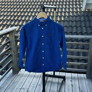 Blårutig skjorta från Lindex Kids 146 - Snygg blårutig skjorta från Lindex Kids i storlek 146. Skjortan har klassisk krage, vita knappar och långa ärmar. Tillverkad i mjuk bomull och passar perfekt för dig som gillar en stilren look med lite edge.