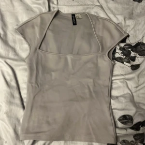 Ljusgrå topp från H&M Divided - Säljer en ljusgrå topp från H&M Divided i storlek XXS. Toppen har korta ärmar och en snygg fyrkantig urringning som ger en modern vibe. Tillverkad i mjukt material som känns skönt mot huden och passar perfekt till jeans eller kjol.