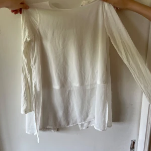 Vit långärmad blus från H&M - Säljer en vit, tunn och flowy blus från H&M i storlek 146. Blusen har långa ärmar, rund halsringning och en snygg slits baktill med knappstängning i nacken. Perfekt för en clean och stilren look.