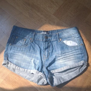 Blå jeansshorts  - Snygga blå jeansshorts från Hun Denim med klassisk femficksdesign och uppvikta benslut. Shortsen har normal passform, bälteshällor och stängs med knapp och dragkedja. Str 170
