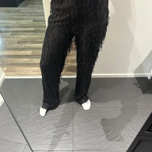 Svarta paljettbyxor med fransar  - Säljer ett par svarta byxor från H&M i storlek S, täckta med glittrande paljetter och fransar för extra partyvibe. Byxorna har rak passform och elastisk midja. Helt oanvända med prislapp kvar 