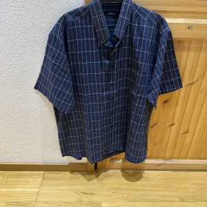 Mörkblå rutig kortärmad skjorta - Snygg mörkblå skjorta med vitt och rött rutmönster. Skjortan har korta ärmar, klassisk krage och knäppning framtill. 