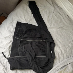 Svart bomberjacka i satin, stl 36 - Svart bomberjacka i glansigt satinliknande material med långa ärmar och dragkedja framtill. Jackan har ribbade muddar vid ärmslut och nederkant för en klassisk look. Perfekt för dig som vill ha en stilren och enkel jacka med lite edge.