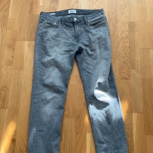 Grå jeans Jack & Jones Regular Clark - Snygga grå jeans från Jack & Jones i modellen Regular Clark. Klassisk femficksdesign, raka ben och normal passform. Jeansen har en cool tvättad look och är tillverkade i mjukt bomullsmaterial med lite stretch för extra komfort.