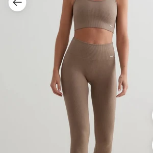 Ribbade beige leggings med hög midja - Snygga ribbade leggings i beige med hög midja och tight passform. Perfekta för träning eller chill, tillverkade i stretchigt material som sitter skönt och formar sig efter kroppen. Stilren look med diskret logga vid höften.