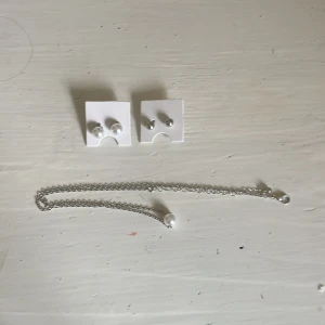 Set med pärlörhängen och halsband - Säljer ett smyckeset med två par örhängen, ett par med vita pärlor och ett par i silverfärgad metall, samt ett matchande halsband med en vit pärla på tunn silverfärgad kedja. Ej äkta. 60 kr för alla eller 20 kr styck. 