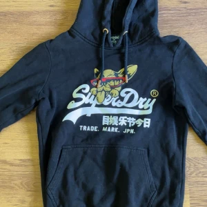 Svart Superdry hoodie med tryck - Svart hoodie från Superdry med coolt tryck. Strl 38, toppenskick!