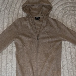 Beige kashmirhoodie Galeries Lafayette - Mjuk och lyxig beige hoodie i 100% kashmir från Galeries Lafayette. Tröjan har dragkedja framtill, huva med snörning och långa ärmar. Perfekt för dig som vill ha en stilren och bekväm look med exklusiv känsla. Storlek S😊