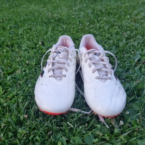 Adidas Copa vita fotbollsskor - Säljer ett par Adidas Copa fotbollsskor i vitt med svarta och röda detaljer. Skorna har klassisk snörning, rund tå och platt sula med orange dobbar. Ovandelen är i skinn för bästa bollkänsla och komfort. Perfekta för dig som vill sticka ut på planen i äkta skin! Använda 1 gång säljer dem då dem e för stora.