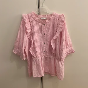 Rosa blus - Jättefin kortärmad blus med knappar och volanger på framsidan, perfekt nu till sommaren💖💐☀️Provade blusen en gång men annars helt ny utan prislapp💞Blusen är storlek L men skulle säga att den passar även s och m💗