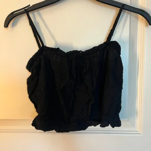 Svart linnetopp med spets och volang - Säljer ett svart linne med spets och volang i storlek 34, använd ett fåtal gånger