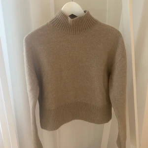 Beige mohairtröja från & Other Stories storlek XS - Stickad tröja från & Other Stories i mohairmix. Tröjan har hög ribbad krage och breda ribbade muddar nedtill och vid ärmslut. Jättebra skick, helt ny med lappar kvar. Storlek XS.