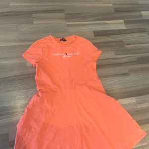 Orange kortklänning Tommy Hilfiger - Superfräsch orange kortklänning från Tommy Hilfiger med rund hals och korta ärmar. Klänningen har tryckt logga framtill och är gjord i mjuk bomull, perfekt för en chill sommardag. Enkel och snygg passform som känns både sportig och trendig. BARNKLÄDER 12-14 år