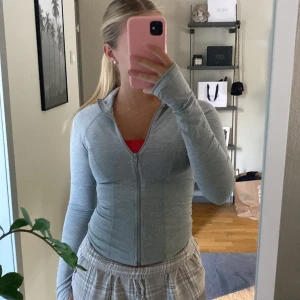 Ljusgrå zip hoodie med tumhål - Superskön ljusgrå hoodie med dragkedja och långa ärmar med tumhål. Sitter tight och har en sportig vibe, perfekt till träning eller chill. Mjuk och stretchig i bomullsmix, enkel design utan mönster eller logga. Aldrig använd, avriven prislapp därav säljer jag den då jag ej kan lämna tbx. 