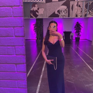 Marinblå långklänning med slits - Säljer en marinblå långklänning med sweetheart-urringning och smala axelband. Klänningen har en snygg slits på ena sidan och figurnära passform som framhäver siluetten. Perfekt för bal eller student! Materialet känns mjukt och följsamt.