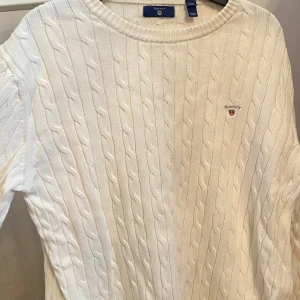 Vit tröja från GANT - Vit tröja från GANT med broderad logga på bröstet. Klassisk rund halsringning och ribbade muddar. Perfekt för dig som gillar en clean och tidlös stil. Skön och mjuk känsla tack vare det stickade materialet. Storlek är 170 cm (15 år) men passar både S och M.