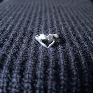 Mains d’Amour – Hands of Love Ring - Justerbar ring i rostfritt stål, rost- och nickelfri. Två händer förenas och formar ett hjärta som omsluter fingret med en varm, symbolisk känsla.