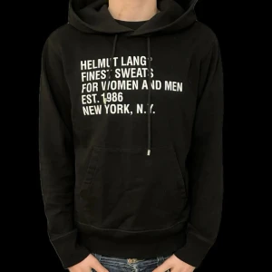 Svart Helmut Lang hoodie med tryck - Svart hoodie från Helmut Lang med vit text på bröstet. Klassisk känguruficka, snörning i huvan och lång ärm. Perfekt för dig som gillar streetstyle och vill ha något bekvämt men ändå snyggt.