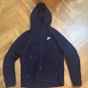 Svart Nike hoodie med dragkedja S - Svart hoodie från Nike med vit logga på bröstet. Tröjan har hel dragkedja, två fickor framtill och en klassisk huva. Perfekt för chill eller träning, i mjukt material och med lång ärm. Snygg och enkel design som funkar till det mesta.