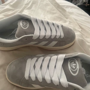 Adidas Campus grå/vita sneakers mocka - Snygga Adidas Campus sneakers i ljusgrå mocka. Pris kan diskuteras i dm. Köpte dem men ångra köpet 1 vecka senare och hade kastat kvitto matchar helt enkelt inte min stil/garderob