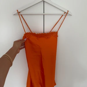 Orange linnetopp med spets från Bik Bok - Superfin orange linnetopp från Bik Bok med tunna axelband som korsas i ryggen och spetsdetalj längs urringningen. Sidenliknande material ger en lyxig känsla och toppen är perfekt för sommarens alla tillfällen. Säljes med prislapp kvar!