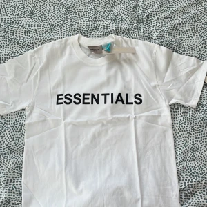 Vit Essentials t-shirt med tryck - Vit t-shirt från Essentials med svart tryck över bröstet. Klassisk rund halsringning och korta ärmar. Skön passform och tillverkad i mjuk bomull. Perfekt för en clean och stilren look.
