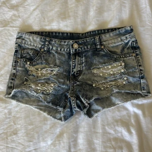 Blå jeansshorts med pärldetaljer - Snygga blå jeansshorts från Amisu med slitna detaljer och pärlor på framsidan. Shortsen har råa kanter, klassisk femficksmodell och cool tvättad look. Perfekta för sommarens alla äventyr om du vill sticka ut lite extra.