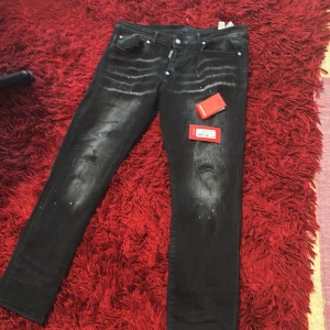 Svarta Dsquared2 jeans med slitningar - Riktigt snygga svarta jeans från Dsquared2 med coola slitningar och färgstänk. Jeansen har en smal passform och klassisk femficksdesign. Märkeslapp vid gylfen och detaljer som ger en edgy vibe. Perfekta för dig som vill sticka ut med din stil.