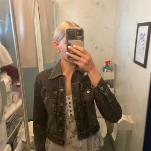 Mörkgrå kort jeansjacka från Labella - Säljer en mörkgrå jeansjacka från Labella i klassisk modell med krage, knappar framtill och två bröstfickor. Perfekt att slänga över en topp för en cool look! Säljs då den var för kort i armarna för mig! Strl: M men sitter som S/xs