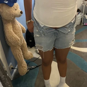 Ljusblå slitna jeansshorts - Säljer ett par ljusblå jeansshorts med slitna detaljer och fransig kant. Shortsen har klassisk femficksdesign, dragkedja och knapp framtill samt en relaxed fit. Perfekta för varma dagar när du vill ha en chill och trendig look.