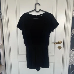 Svart playsuit från BikBok - Svart playsuit från BikBok i storlek S med korta ben och resår i midjan. Enkel och stilren design med rund halsringning och kort ärm. Perfekt för varma dagar när du vill ha något bekvämt men ändå snyggt.