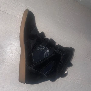 Svarta sneakers med kardborre och mockadetaljer - Snygga svarta sneakers med högt skaft och coola kardborreband. Skorna har en mix av mocka och syntet, samt en kontrasterande ljusbrun sula. Den är i storlek 42 men liten i storlek sulan är 26,5 cm. De är inte de äkta isabel marant men skulle påstå att de är identiska. Helt nya och oanvända säljer pgd av att de är för små. Skriv om ni vill ha fler bilder eller om ni har ytterligare frågor💗💗