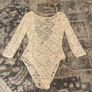 Beige spetsbody med blommönster - Säljer en superfin beige body i spets med blommigt mönster. Den har djup rundad ringning och trekvartsärmar. Perfekt att styla med jeans eller kjol för en trendig look. Spetsen ger en romantisk vibe och den är riktigt bekväm att bära.