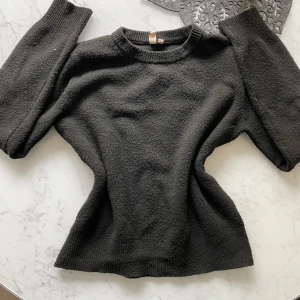 Svart stickad tröja från Nelly  - Säljer en svart stickad tröja med rund halsringning. Tröjan har en klassisk passform och ribbade muddar vid ärmslut och nederkant. Perfekt för kyliga sommarkvällar 