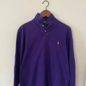Lila långärmad pikétröja från Polo Ralph Lauren - Säljer en lila långärmad pikétröja från Polo Ralph Lauren. Skick 9/10 finns inget som antyder att den är använd. Storlek M. Tröjan har den ikoniska gula loggan broderad på bröstet. Perfekt för en stilren och avslappnad look.