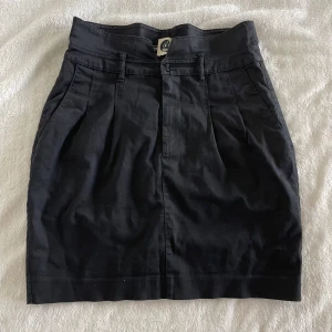Svart kjol från cheap monday - Svart kjol från Dr Denim med hög midja, bälteshällor och två fickor bak. Kjolen har en rak passform. Klassisk design med slits bak för extra rörelsefrihet. Underkjolen är trasig (sista bilden) Midja: 36cm, Längd: 49cm