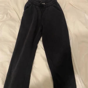 Svarta mjukisbyxor med NYC-brodyr från H&M - Svarta mjukisbyxor från H&M med broderad NYC-detalj på ena benet. Byxorna har resår i midjan med dragsko och är tillverkade i mjukt bomullsmaterial. Perfekta för en avslappnad stil. I storlek 158