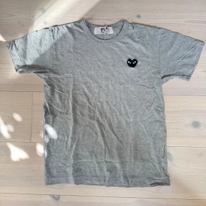 Grå T-shirt från Comme des Garçons - Grå t-shirt från Comme des Garçons Play med dem klassiska hjärt-loggan. Bättre skick än vad det ser ut som på bilden, lite skrynklig pga förvaringen bara! 