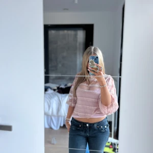 Rosa blus med spets och volang - Säljer en söt rosa blus med transparenta partier och spetsdetaljer. Blusen har trekvartsärm och är croppad med volang längs ärmar och nederkant. Perfekt för dig som gillar romantisk stil!